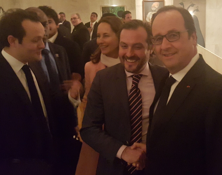 Groupe de personnes en costume souriantes lors d'un événement formel, en train de se serrer la main