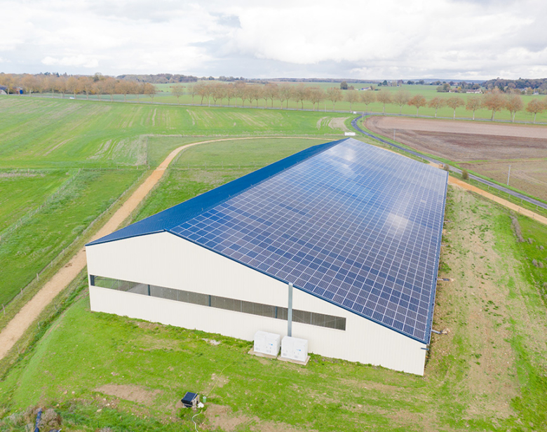 Bâtiment agricole avec toit équipé de panneaux solaires dans un paysage rural verdoyant