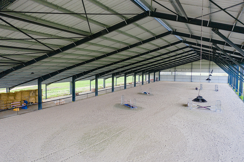 Salle couverte d'entraînement équestre avec sol en sable et divers obstacles pour le dressage des chevaux