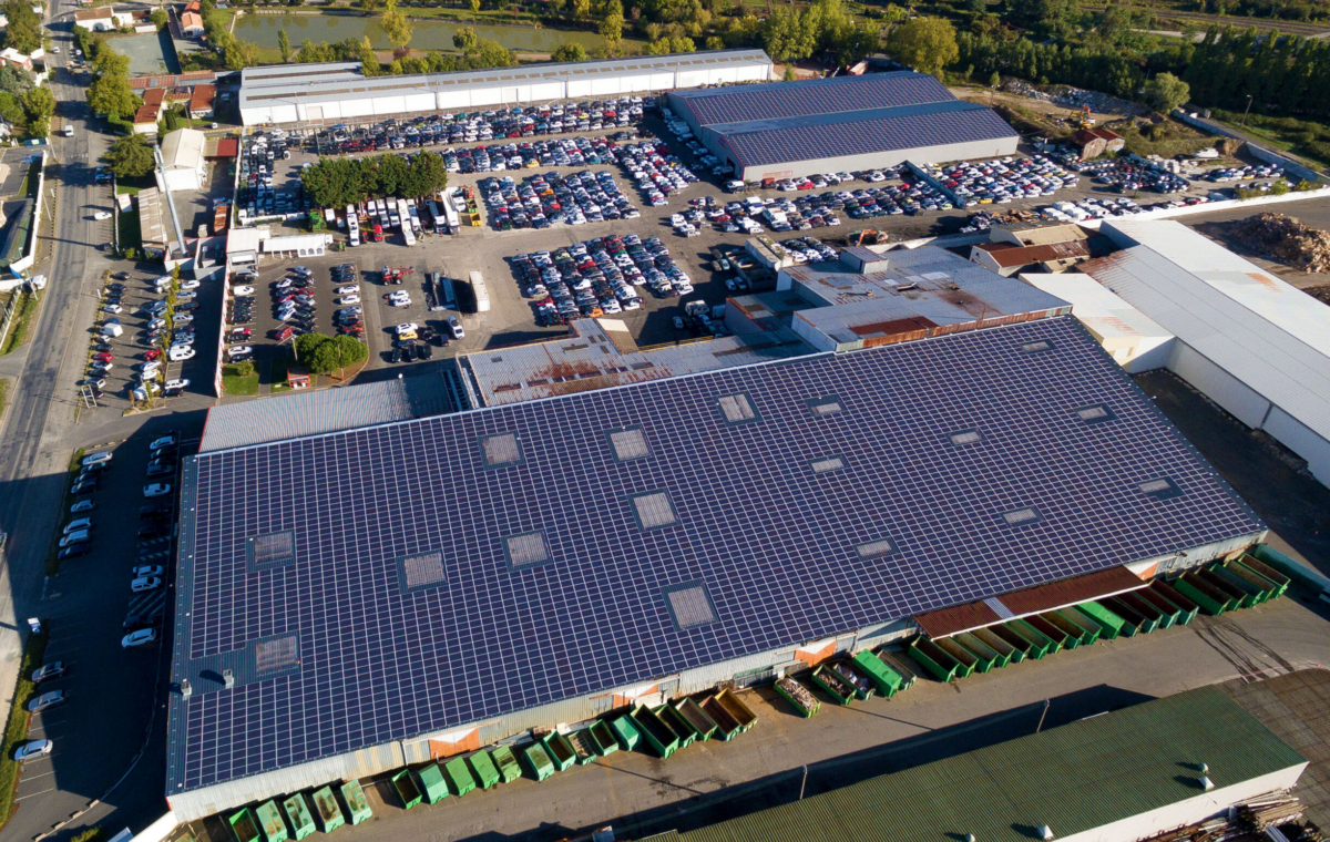 Vue aérienne d'un grand parking avec de nombreux véhicules et bâtiments industriels équipés de panneaux solaires