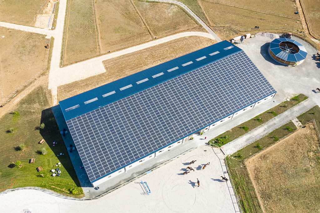 Bâtiment industriel avec panneaux solaires et structure circulaire adjacente dans un environnement rural