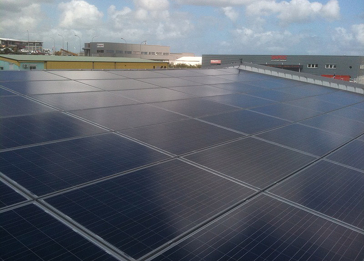 Installation de panneaux solaires sur un toit industriel avec bâtiments et parking en arrière-plan