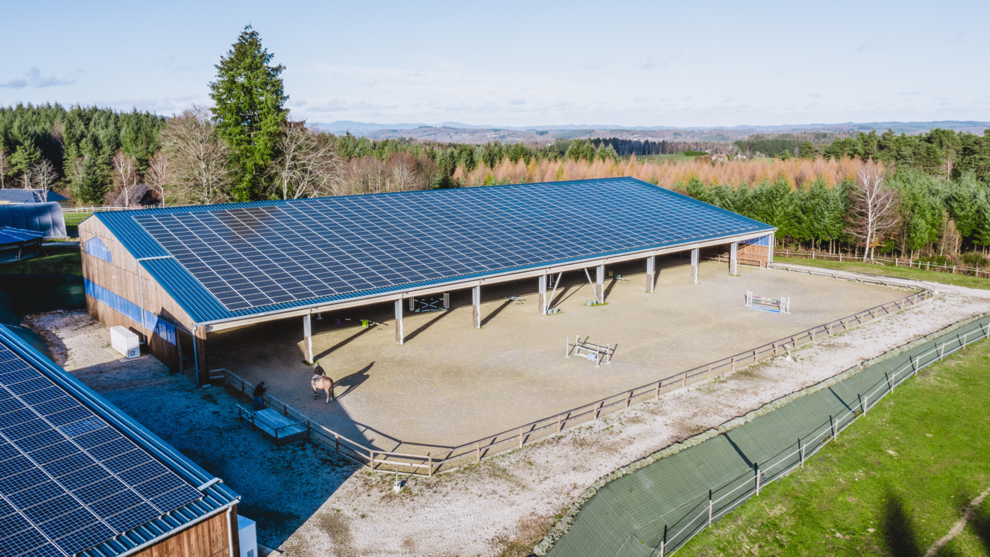 Centre équestre moderne avec une grande structure abritée équipée de panneaux solaires intégrés en toiture photovoltaï