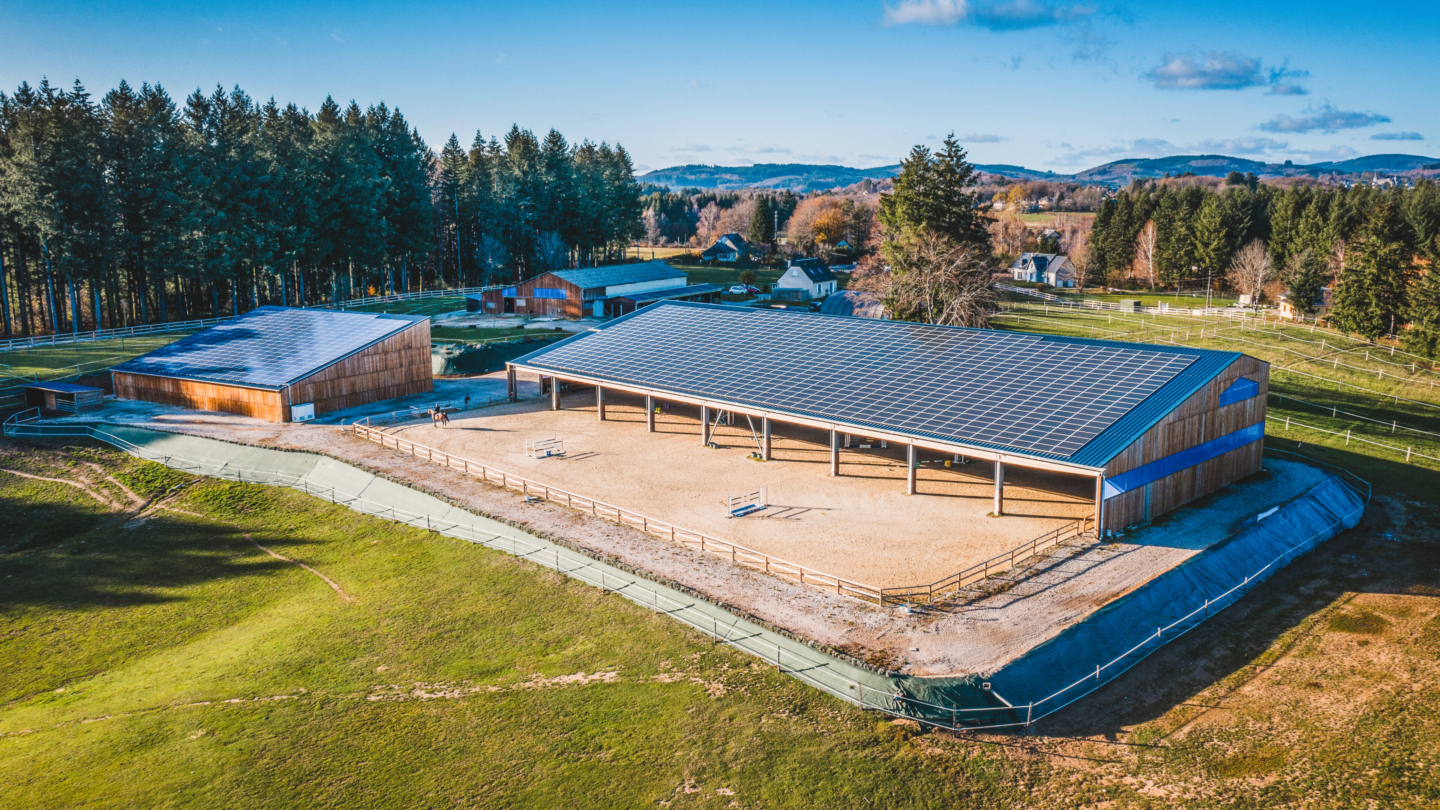 Installation équestre moderne avec toitures photovoltaïques intégrées dans un cadre naturel boisé et vallonné offrant u