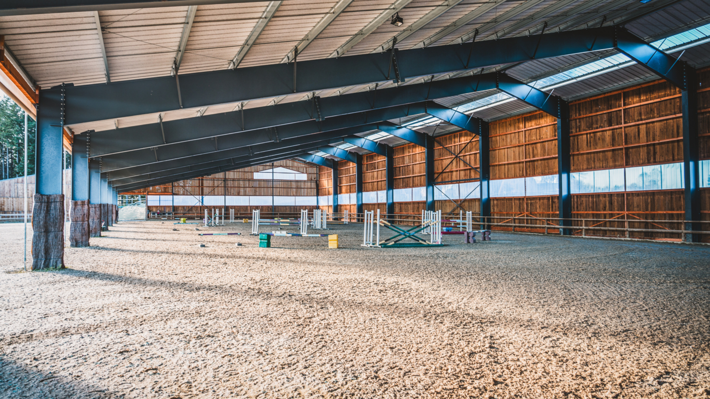 Salle de sport équestre couverte avec sol en gravier et obstacles pour dressage et entraînement d'équitation sous une stru