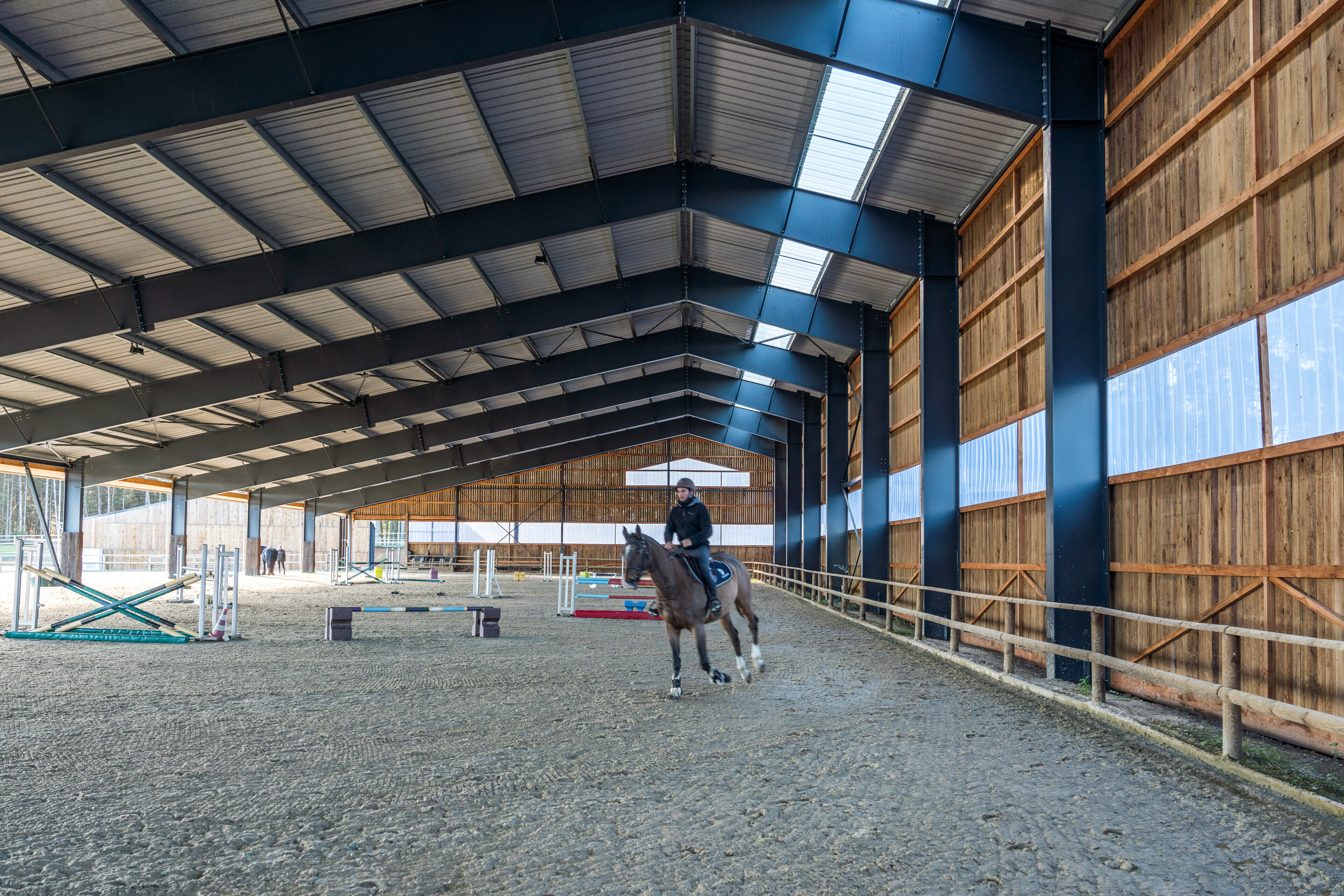 Salle d’équitation moderne avec structure en bois et éclairage naturel optimisé par des skylights
Un cavalier entraîne