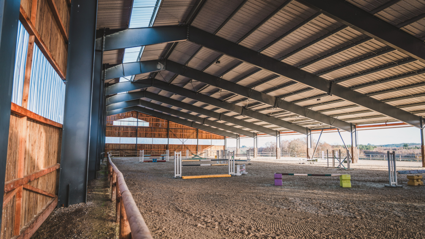 Salle d'entraînement équestre moderne avec structure en bois et toiture industrielle spacieuse idéale pour les installatio