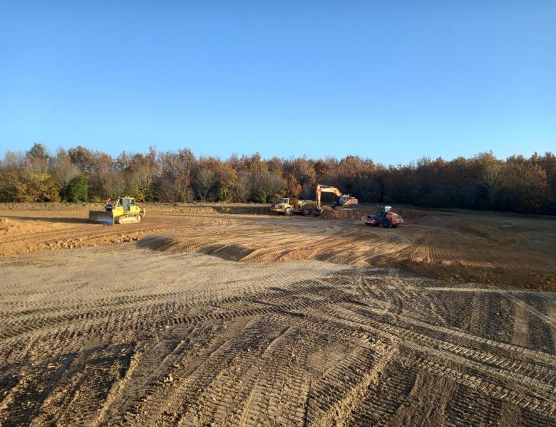 Chantier de construction avec engins de terrassement et terrain en cours de nivellement entouré de végétation automnale
