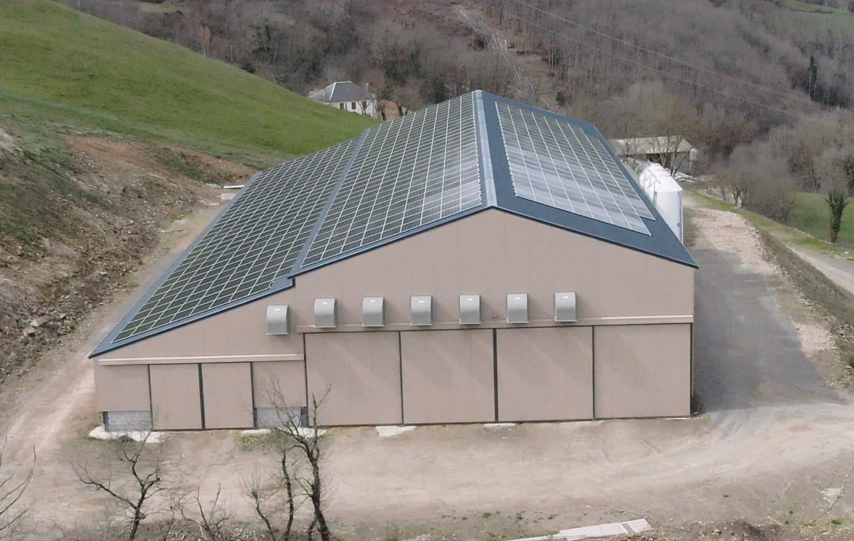 Bâtiment agricole avec toit équipé de panneaux solaires en pleine campagne entourée de collines et de forêts