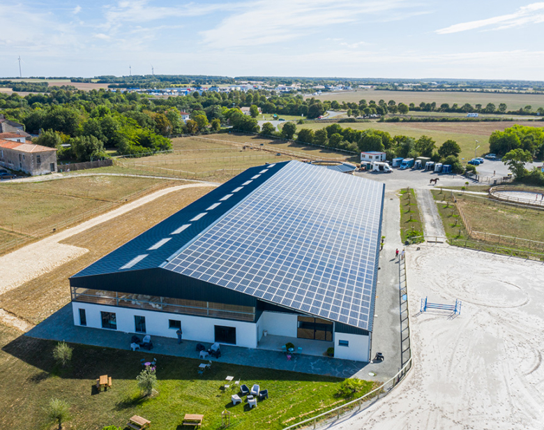 Bâtiment moderne avec toit solaire entouré de terrains agricoles et d'espaces verts, incluant une piste d'équitation et de
