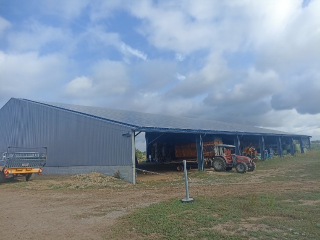 Bâtiment agricole couvert avec tracteur et remorque chargée de foin sur terrain en extérieur