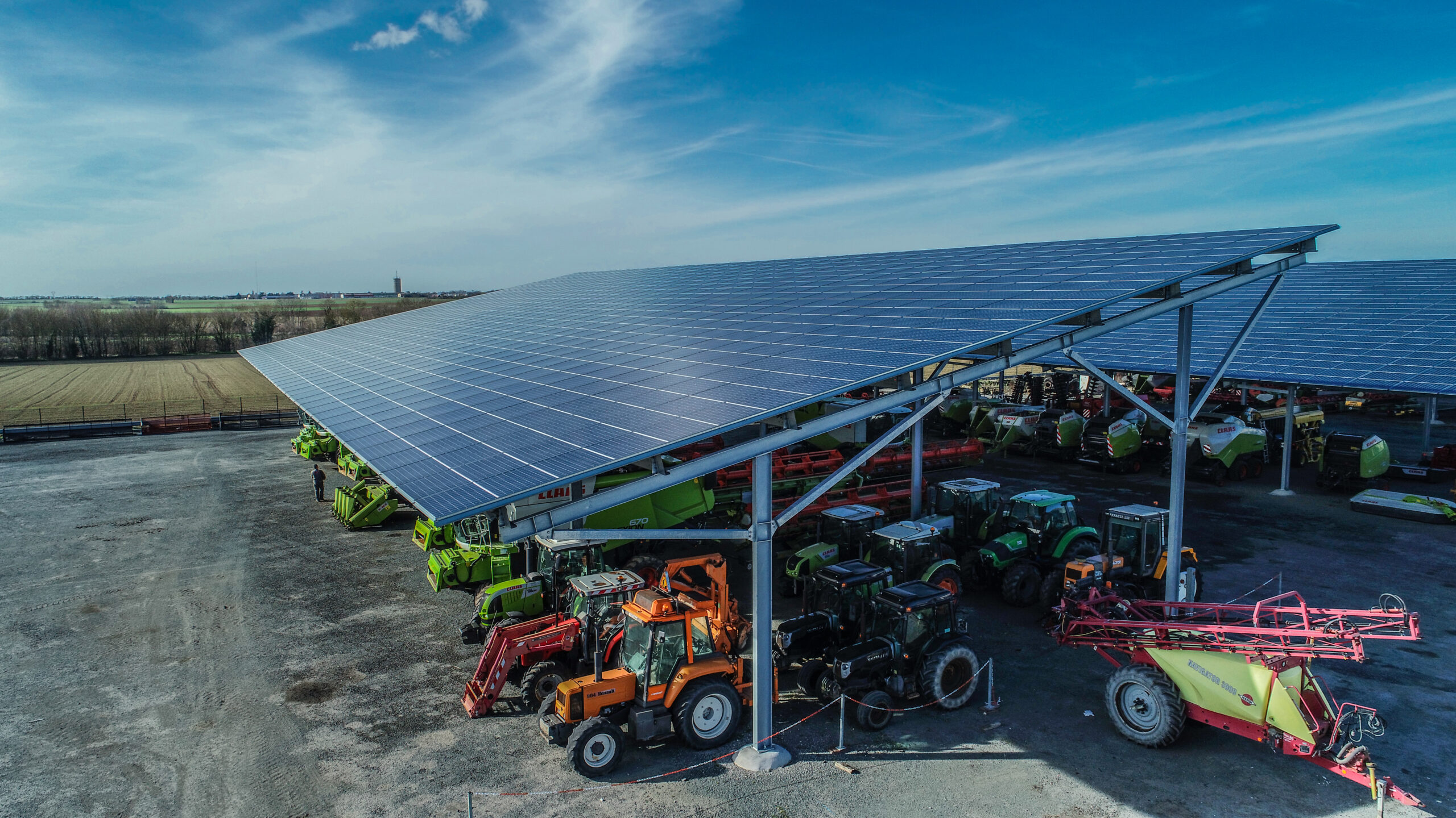 Parking de machines agricoles couvert par des panneaux solaires avec vue sur des champs en arrière-plan