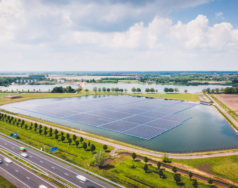 Vue aérienne d’un champ solaire flottant près d’une route avec paysage verdoyant et lac à l’arrière-plan