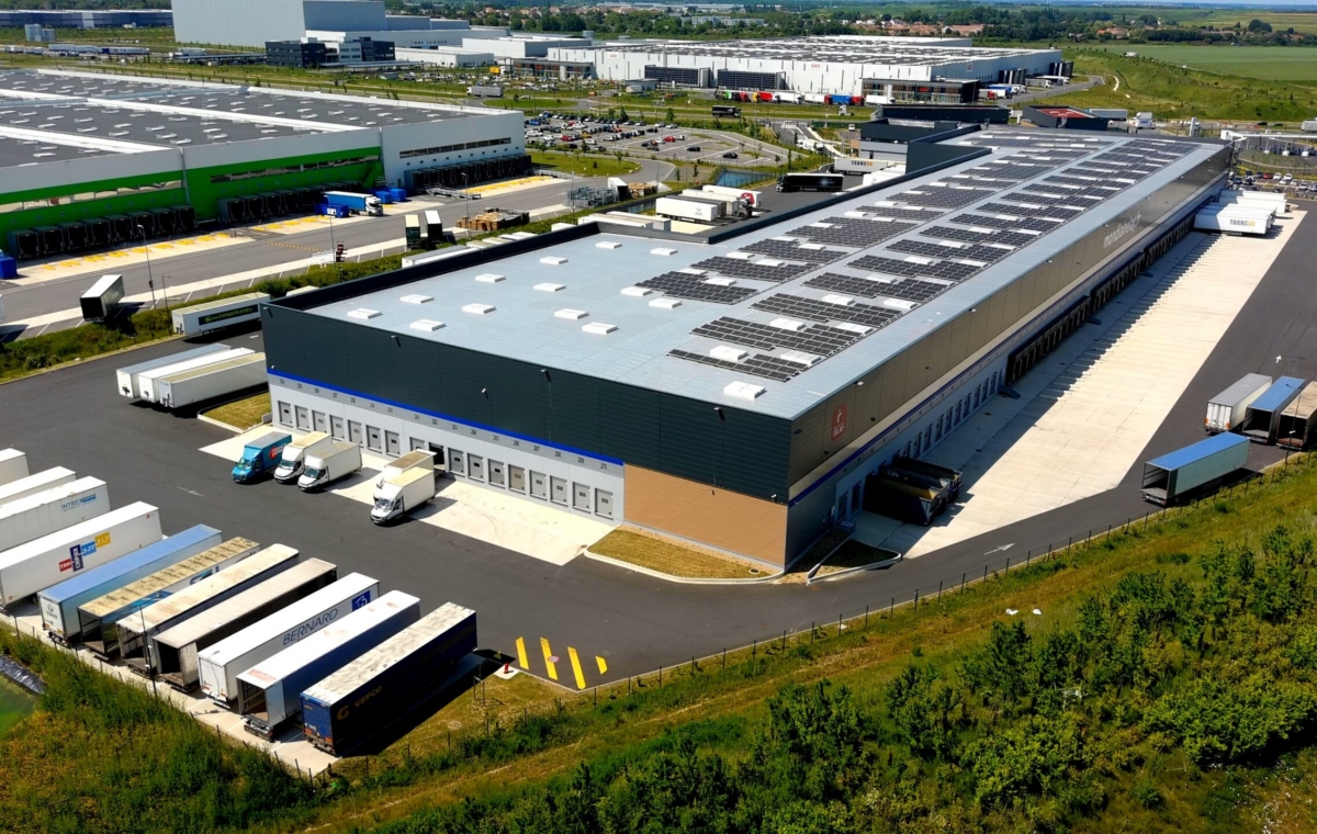 Vue aérienne d'un grand entrepôt industriel avec panneaux solaires sur le toit et plusieurs camions de livraison