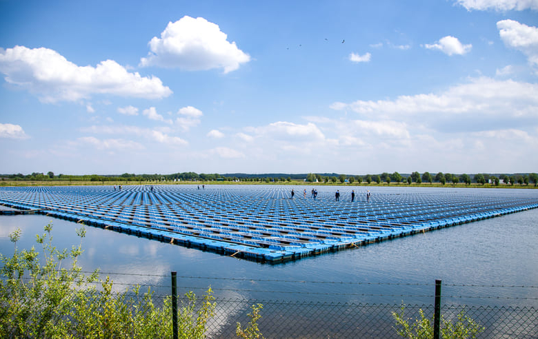 Pisciculture avec bassins remplis d’eau et filets de culture flottants sous un ciel dégagé, vue depuis une zone verte ave