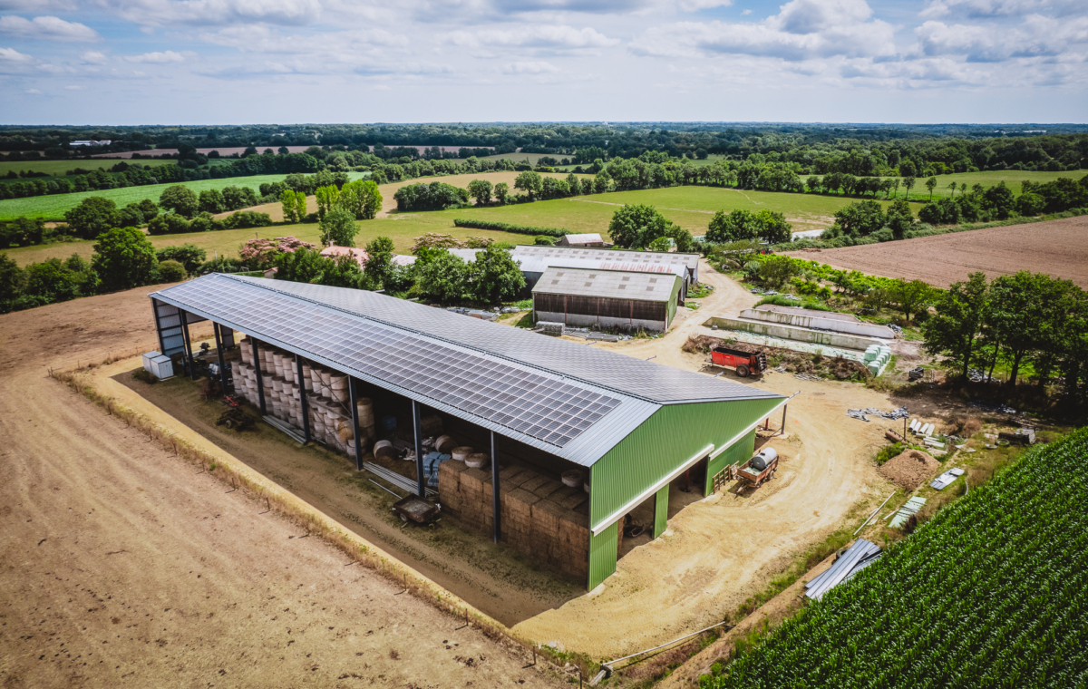 Ferme moderne équipée de toiture photovoltaïque intégrée dans un paysage agricole verdoyant avec champs environnants et