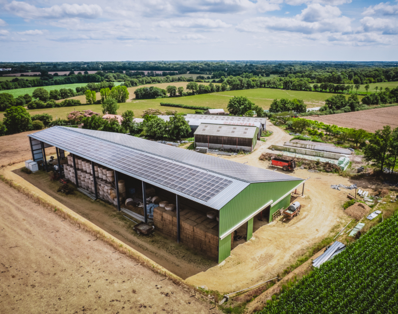 Ferme moderne équipée de toiture photovoltaïque intégrée dans un paysage agricole verdoyant avec champs environnants et