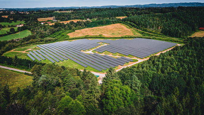 Parc solaire installé dans une zone verte entourée de forêts et de champs, vue aérienne