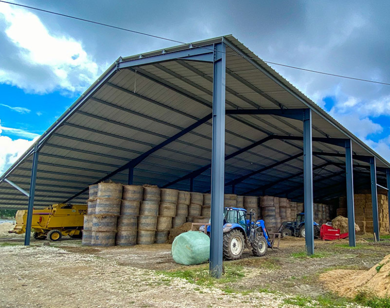 Bâtiment agricole couvert avec empilements de balles de foin et tracteurs à l'intérieur et à l'extérieur