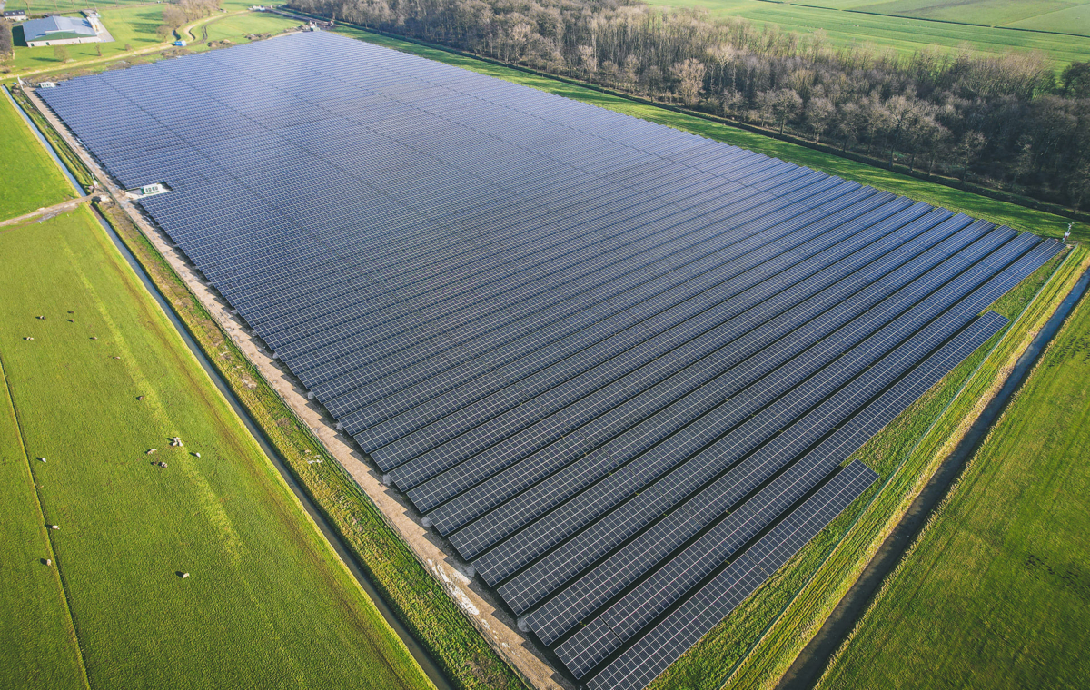 Vue aérienne d'un champ de panneaux solaires disposés sur un terrain agricole entouré de verdure et de forêts