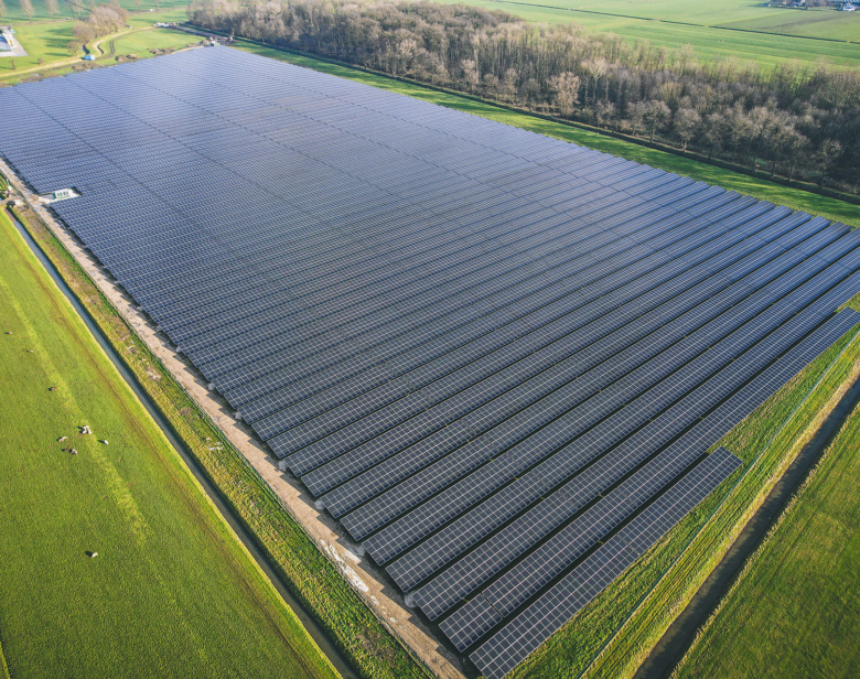 Vue aérienne d'un champ de panneaux solaires disposés sur un terrain agricole entouré de verdure et de forêts