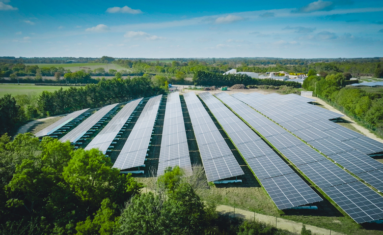 Parc solaire composé de nombreux panneaux photovoltaïques alignés dans un paysage rural avec végétation et ciel dégagé