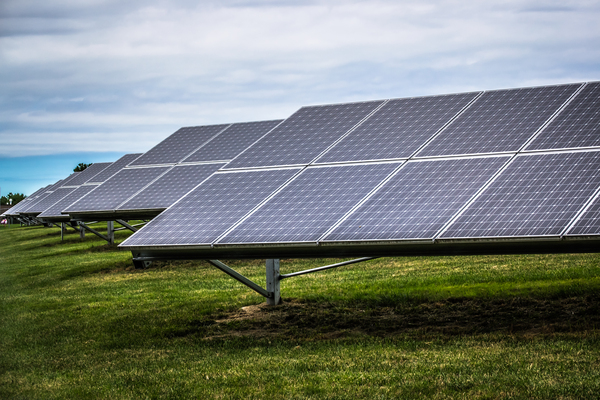 Ensemble de panneaux solaires photovoltaïques installés sur un terrain herbeux sous un ciel partiellement nuageux