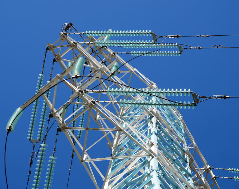 Tour de transmission électrique avec isolateurs et câbles haute tension contre un ciel bleu clair