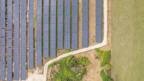 Vue aérienne d’un champ de panneaux solaires alignés dans un paysage agricole avec des zones vertes et des chemins de ter