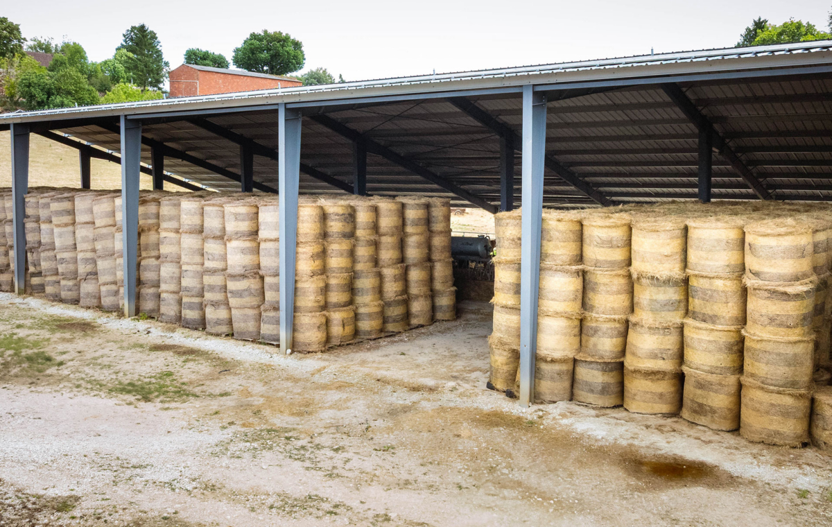 Stockage de balles de foin sous abri métallique avec tracteur visible à l'arrière