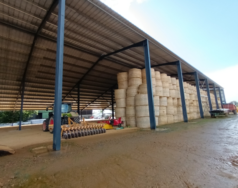 Abri agricole abritant des balles de foin et des tracteurs avec matériel agricole sous une structure métallique et toiture