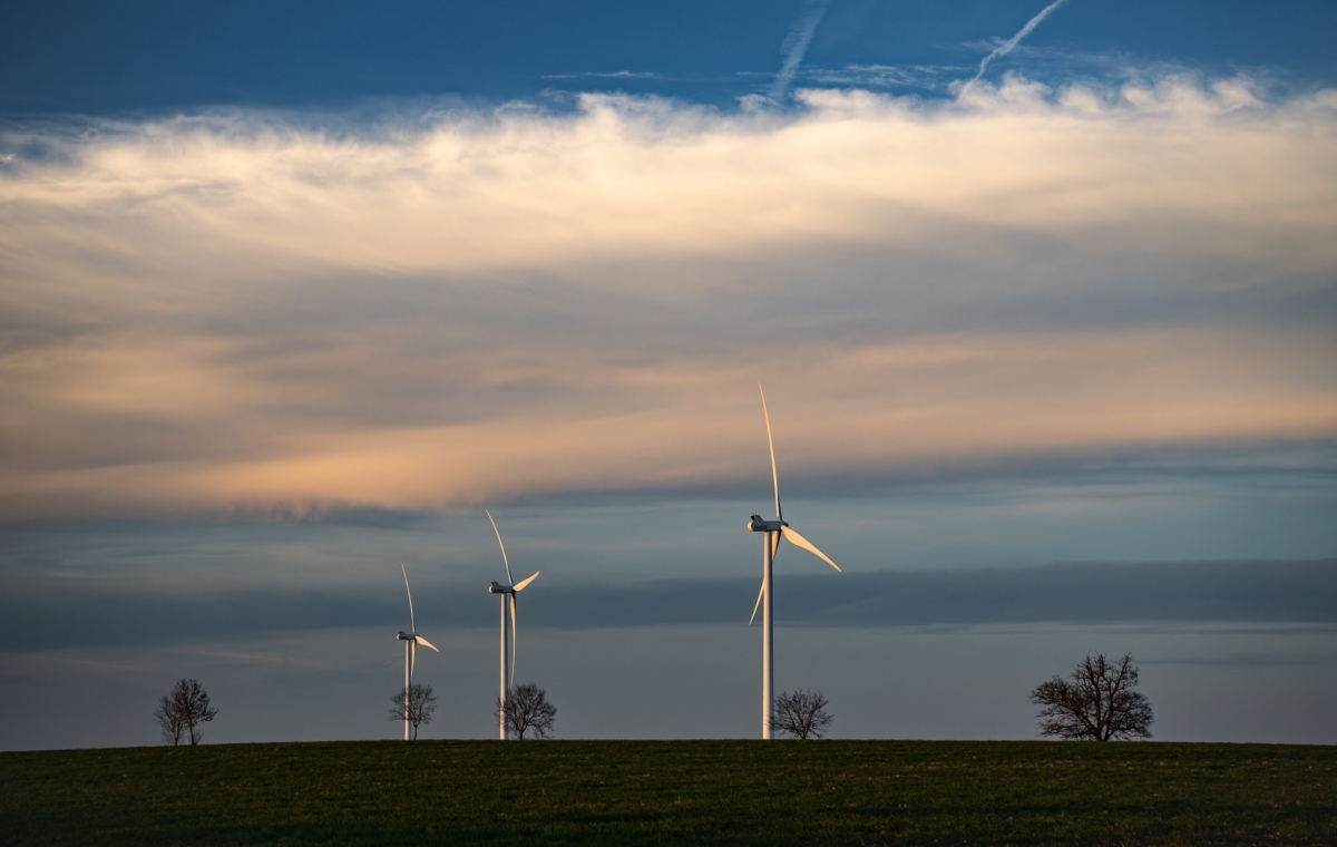 Éoliennes sur un champ au coucher du soleil avec ciel partiellement nuageux et arbres isolés