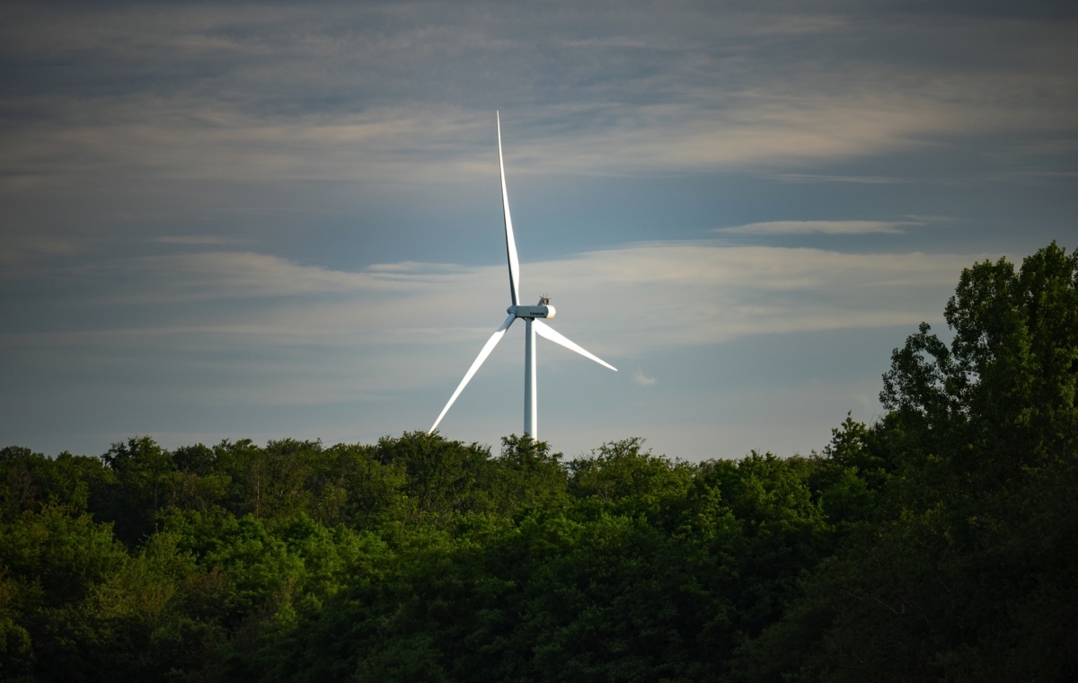 Éolienne moderne se dressant au-dessus d'une forêt dense sous un ciel partiellement nuageux