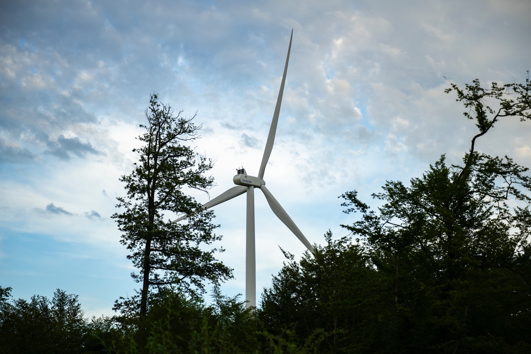Éolienne moderne entourée d'arbres sous un ciel partiellement nuageux