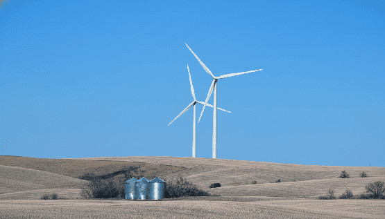 Éolienne sur un champ de cultures sous un ciel dégagé avec des silos à grain au premier plan