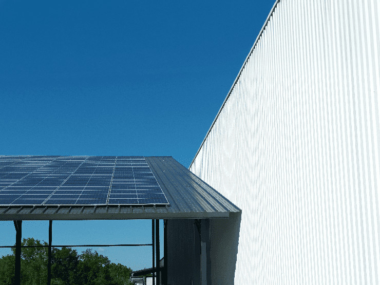 Bâtiment industriel avec panneaux solaires sur toit et façade en tôle ondulée sous ciel dégagé