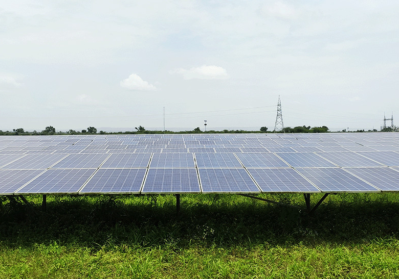 Champ de panneaux solaires photovoltaïques alignés sur terrain vert avec horizon dégagé et lignes électriques à distanc