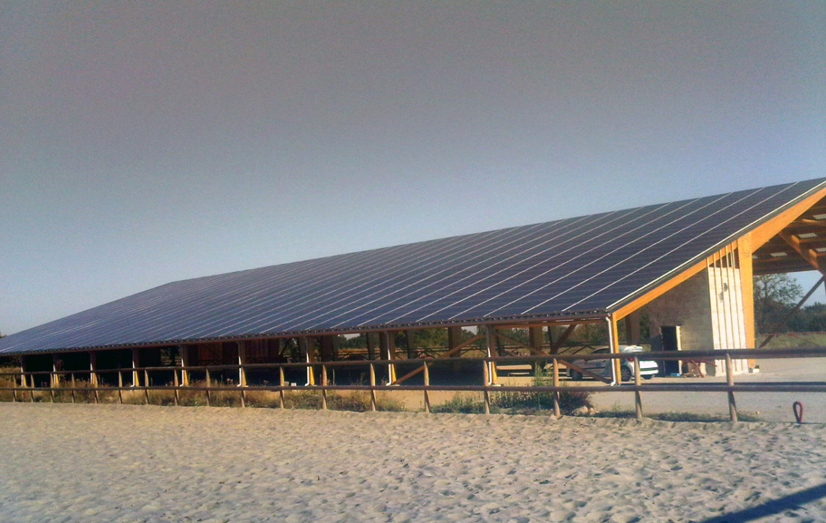 Bâtiment couvert avec toit métallique et structure en bois, situé sur un sol sableux et entouré de barrières en bois