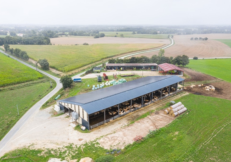 Ferme moderne avec bâtiment d’élevage abrité sous ombrière solaire entourée de vastes champs agricoles et infrastructu