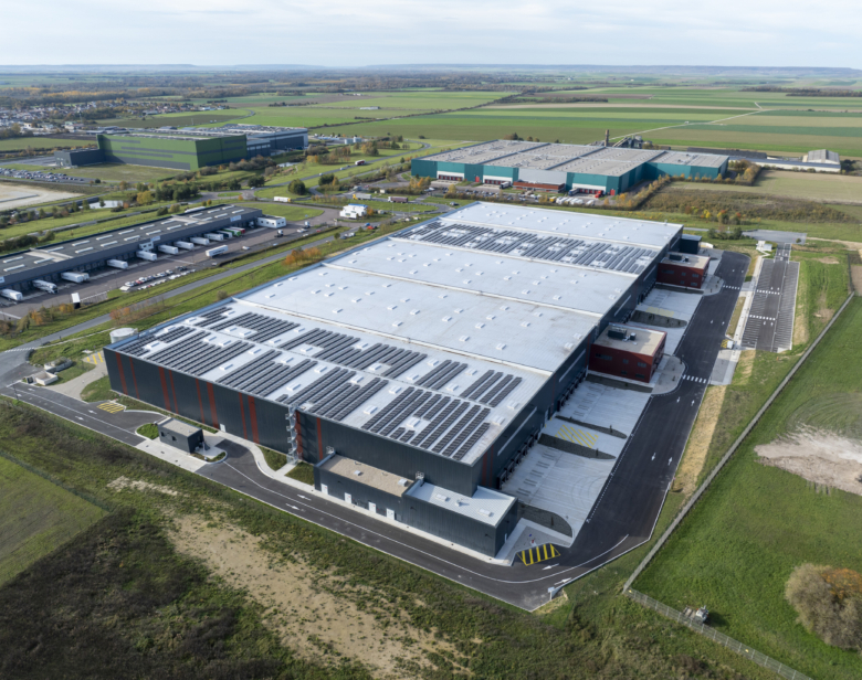 Vue aérienne d’un vaste complexe industriel avec des bâtiments de stockage et des parkings adjacents en zone rurale entou