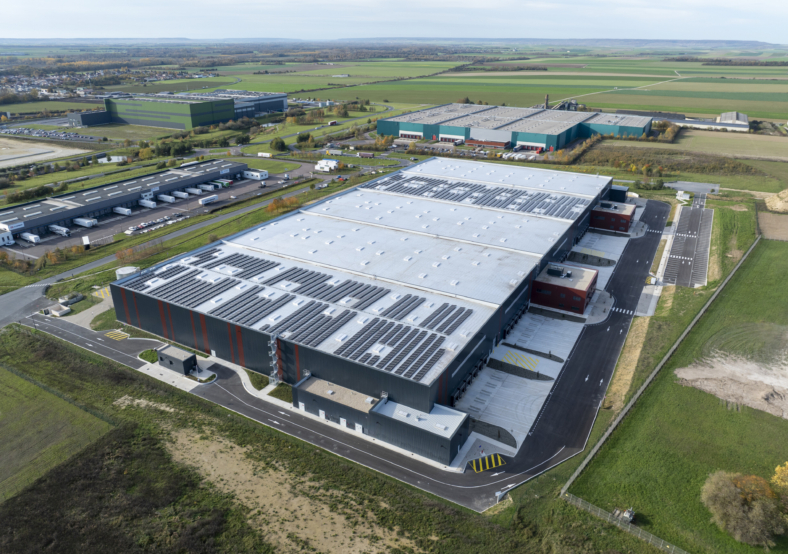 Vue aérienne d’un vaste complexe industriel avec des bâtiments de stockage et des parkings adjacents en zone rurale entou