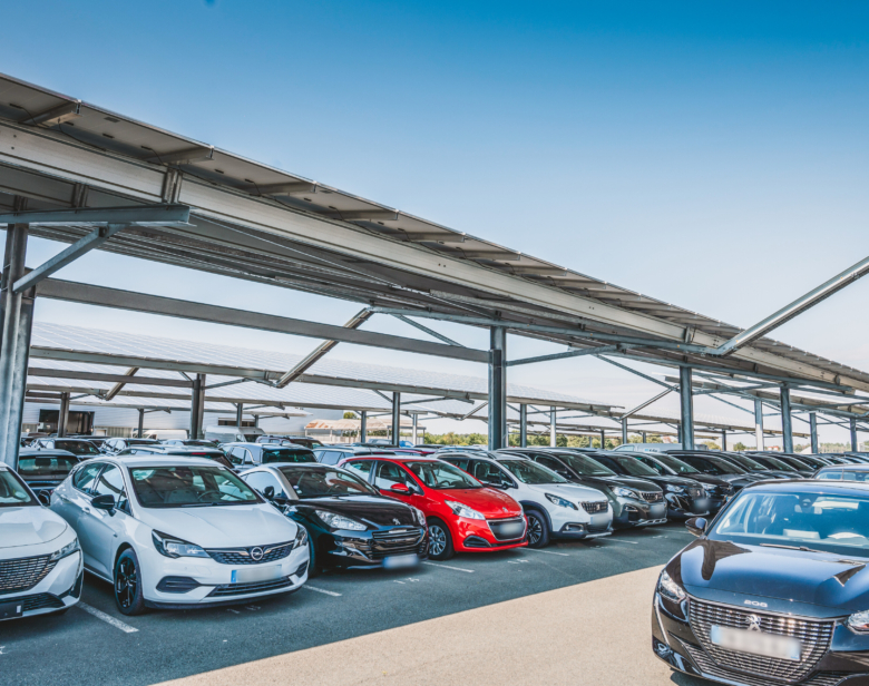Parking couvert avec voitures neuves exposées sous structure métallique et toiture équipée d’ombrières solaires permet