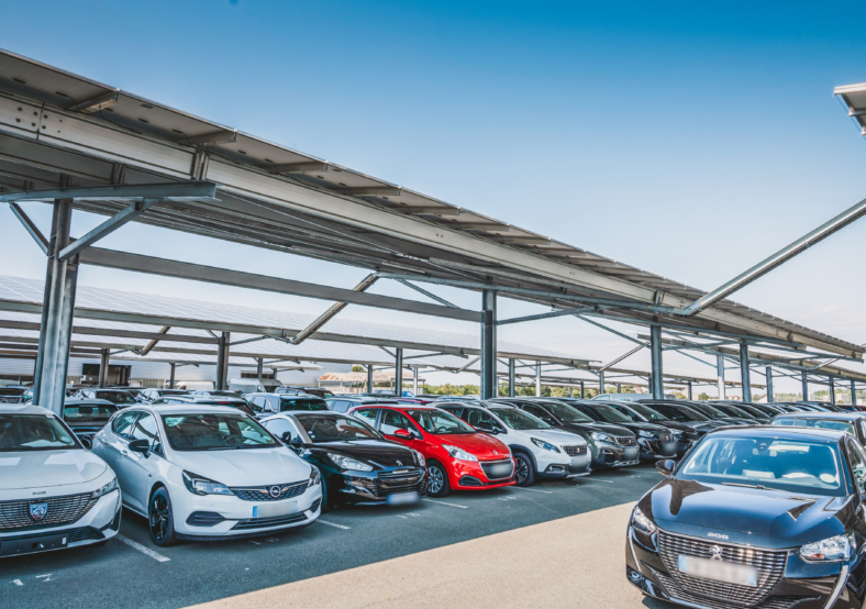 Parking couvert avec voitures neuves exposées sous structure métallique et toiture équipée d’ombrières solaires permet
