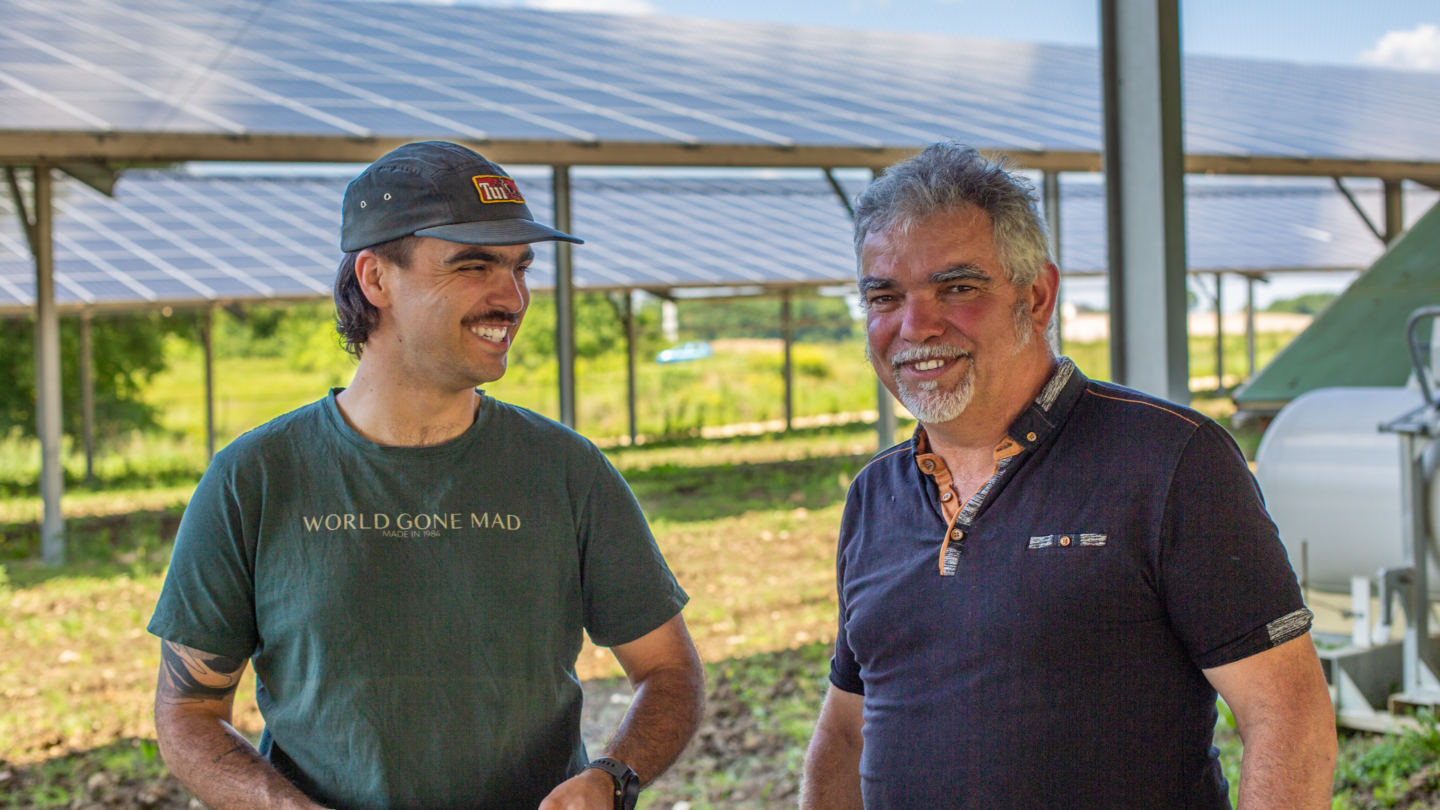 Deux hommes souriants dans une structure agricole innovante combinant cultures et ombrières solaires pour une approche durab