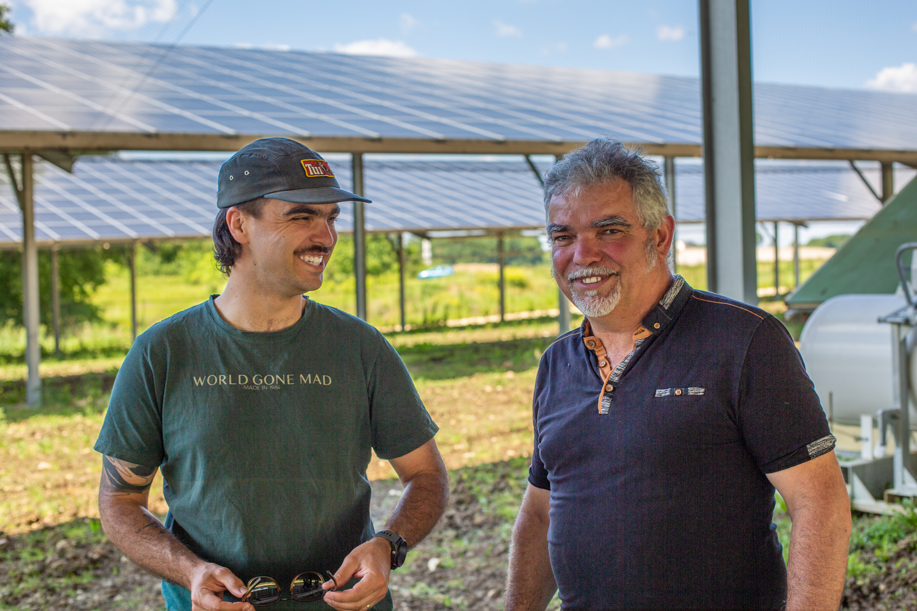 Deux hommes souriants dans une structure agricole innovante combinant cultures et ombrières solaires pour une approche durab