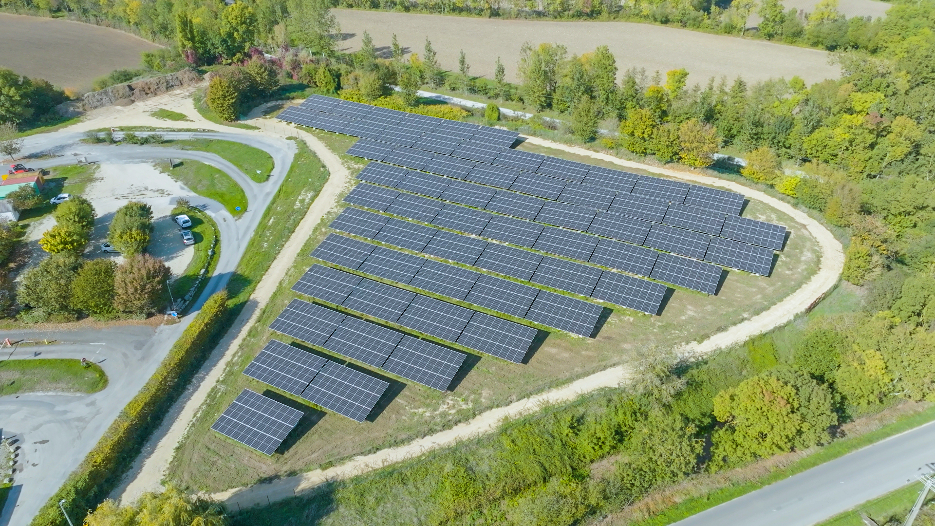 Installation photovoltaïque en plein air sur terrain agricole entourée de végétation et de chemins sinueux illustrant une