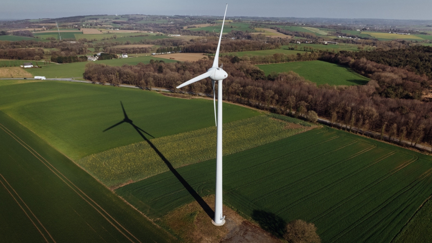 Vue aérienne d’un paysage rural avec des champs agricoles et une imposante éolienne en activité illustrant l’intégrat