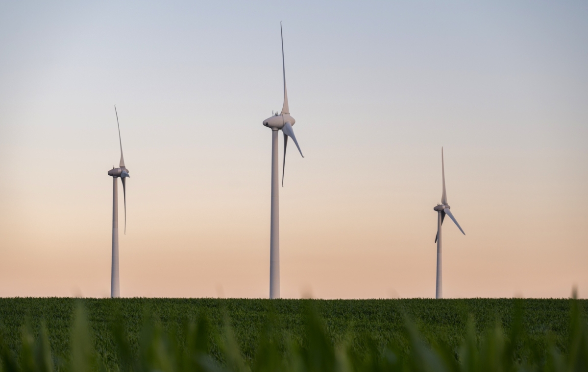 Parcs éoliens en pleine nature avec trois éoliennes modernes s’élevant au-dessus d’un champ vert sous un ciel crépusc