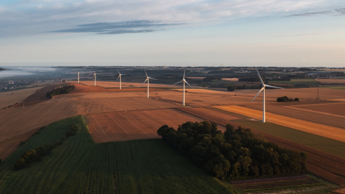 Parc éolien moderne s’étendant dans un paysage agricole vallonné sous un ciel dégagé avec des champs cultivés et des