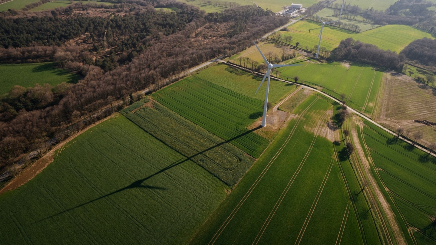 Vue aérienne de paysages ruraux avec champs structurés et éoliennes en activité illustrant une transition énergétique d